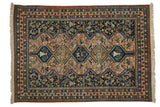 Vintage Persian Ardebil carpet featuring navy and pale peach repeating medallions with stylized figures.