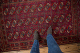 A vintage Turkmen Tekke rug in burgundy red, shown underfoot to display the scale of its gul pattern.