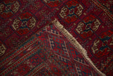 A vintage Tekke rug's corner folded back to show the intricate weave, wool foundation, and side cord selvage.