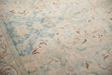 Low-pile texture of a distressed vintage carpet with scrolling vinery in powder blue, ivory, and brown.