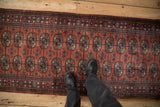 Overhead view of a vintage Bokhara runner's plush dark rose pile and detailed navy gul medallions.