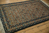 Angled view of a vintage Ardebil rug with a rust and blue lattice pattern and a dark navy border.