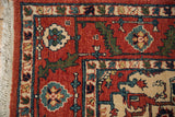 Corner detail of a vintage Indian rug with a serrated leaf border in rust, blue, and green.