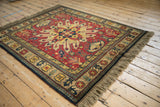 Vintage Kazak rug viewed from an angle, showing its rust-red starburst medallion and thick, full pile.