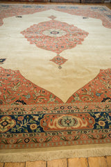 Angled view of a vintage rug's plush ivory pile, dusty blush spandrel, and navy border.
