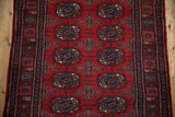 Detailed view of the repeating gul medallions and fine wool pile of a red and navy Bokhara runner.