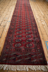 Long vintage Bokhara runner viewed from its fringed end, showing repeating red and navy guls.
