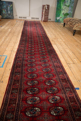 Angled view of a long Bokhara runner highlighting its repeating red and navy gul pattern.