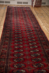 Angled perspective showing the full length of a red Bokhara runner with repeating gul medallions.