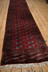 Angled view of a long vintage Bokhara runner showing the repeating gul motif and ivory fringe.