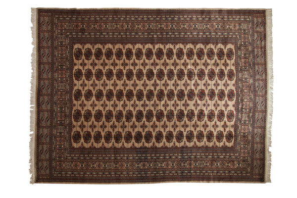 Vintage Bokhara carpet with repeating gul medallions in brown, navy, and bronze on a cream field.