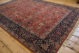 Angled view of a vintage Agra carpet's brick red allover field and intricate navy blue border.