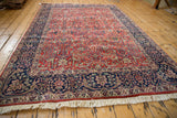 Angled view highlighting the full, plush pile of a vintage Agra carpet in brick red and navy blue.