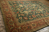 Angled view of a vintage Indian carpet's lustrous green pile and detailed terracotta floral border.