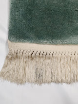 Thick aqua green pile meeting ivory knotted fringe at the rug's secured end.