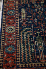 Hand-knotted Bakhtiari rug detail showing navy field with stylized cypress and a brick red palmette border.