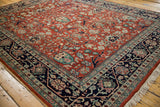 Angled perspective of a vintage carpet's even pile, red floral field, and navy vine border.