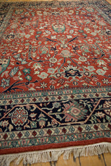 Angled view of a vintage Bijar design carpet's plush red pile, navy border, and fringe.