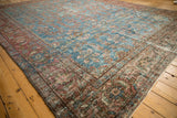 Vintage Persian Mahal carpet close-up with worn aqua field and intricate floral burgundy border.