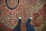 Antique Serapi carpet's low-pile texture with serrated navy medallion and terracotta field.
