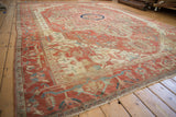 Angled view across an antique Serapi carpet highlighting its grand scale, terracotta field, and ivory patterns.