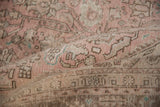 Folded distressed vintage Isparta rug shows geometric vinery, dusty rose, beige, and pale green.