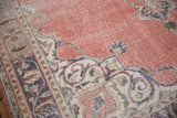 Detail of hand knotted distressed Sparta rug with dusty rose field, beige patterns, and visible wear.