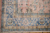 Distressed Sparta carpet corner detail with dusty rose field, blue border, floral palmettes, and wear.