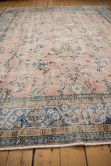 Distressed dusty rose field with faded floral palmettes and a worn blue border.