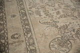 Distressed Tabriz carpet detail: faded floral vinery, geometric border, and soft ivory, charcoal tones.
