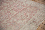 Textural view of a distressed Sparta carpet, faded dusty rose and beige scrolling vinery.