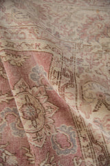 Distressed hand-knotted pile of the Sparta carpet with faded scrolling vinery, pale rose, ivory, and beige.