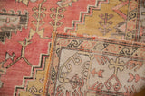 Folded vintage Oushak rug displaying distressed dusty pink geometric patterns and woven foundation.
