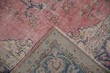Distressed vintage Sparta carpet corner, revealing dusty pink pile, cobalt designs, and woven reverse.