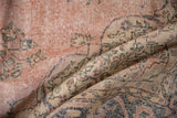 Folded vintage Sparta carpet with faded dusty rose, ivory floral design, visible wear.