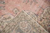 Folded vintage Sparta rug, highlighting distressed light pink pile and floral arabesque border.
