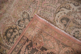 Distressed Oushak rug folded corner, showing muted blush pile and woven reverse with fringe.