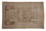 Distressed vintage Oushak carpet with faded coffee brown and beige shield medallion, ram's horn motifs.