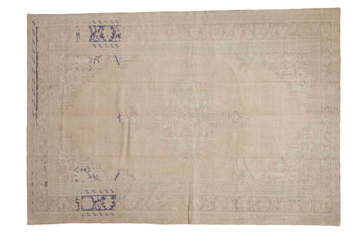 Vintage distressed Oushak carpet in sandy tones with a faint medallion and details in cobalt blue and pale green.