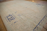 Angled view of a distressed Oushak carpet showing the worn, low pile texture in sandy and pale green tones.