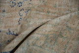Close-up of distressed vintage Oushak rug, showing mostly even wear, ivory, blue, and sage pattern.