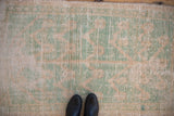 The heavily worn, low-pile texture of a distressed Tulu rug in mint green and soft beige.