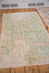 Angled view of a vintage Tulu rug highlighting its distressed, time-softened texture and muted green tones.