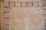 Distressed vintage Oushak rug corner, showing geometric border in beige, dusty mauve, and coffee brown.