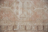 Distressed texture of vintage Oushak rug, muted geometric motifs in beige and dusty mauve.