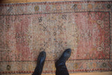 Distressed Oushak rug featuring worn texture in blush and beige, with black boots.