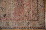 Distressed Oushak rug showing decorative wear, dusty blush and beige floral patterns, and border detail.