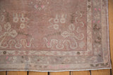 Corner detail of distressed Oushak rug runner, revealing faded rococo motifs, dusty rose, and fringe.