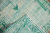 Distressed Oushak rug corner revealing worn green pile, woven foundation, and intact selvage.
