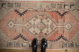 Distressed vintage Oushak rug corner: faded blush, geometric patterns, and black shoes.